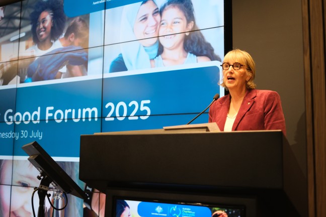 ACNC Commissioner Sue Woodward AM standing at a podium in front of a digital screen