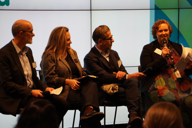 Image of four people sitting on chairs on a stage, at a forum