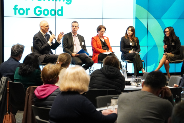 Image of five people sitting on chairs on a stage at a conference.